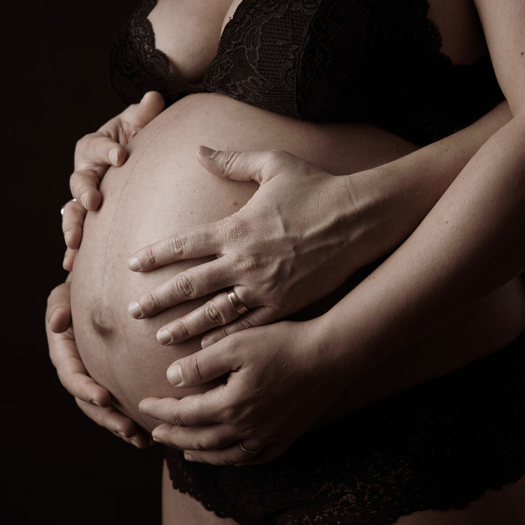 babybauchfoto im Studio fotografiert mit Händen der Eltern auf dem Bauch