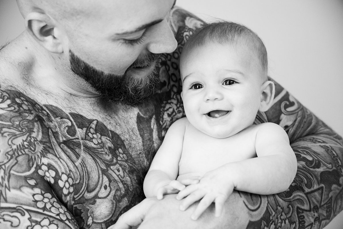 lachendes, süßes babyportrait im Sudio, baby ist bei seinem volltätowierten papa auf dem arm