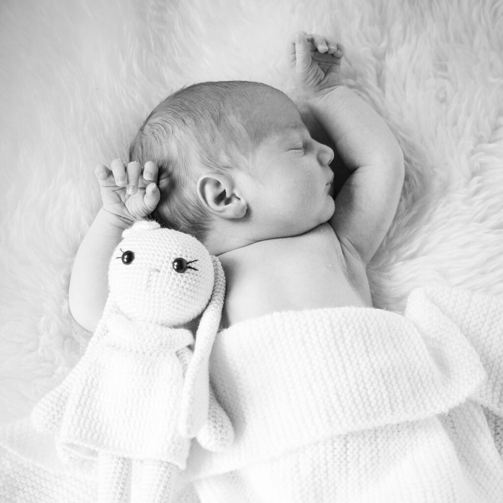 Newbornfoto, neugeborenes auf einem Schaffell mir Kuscheltier