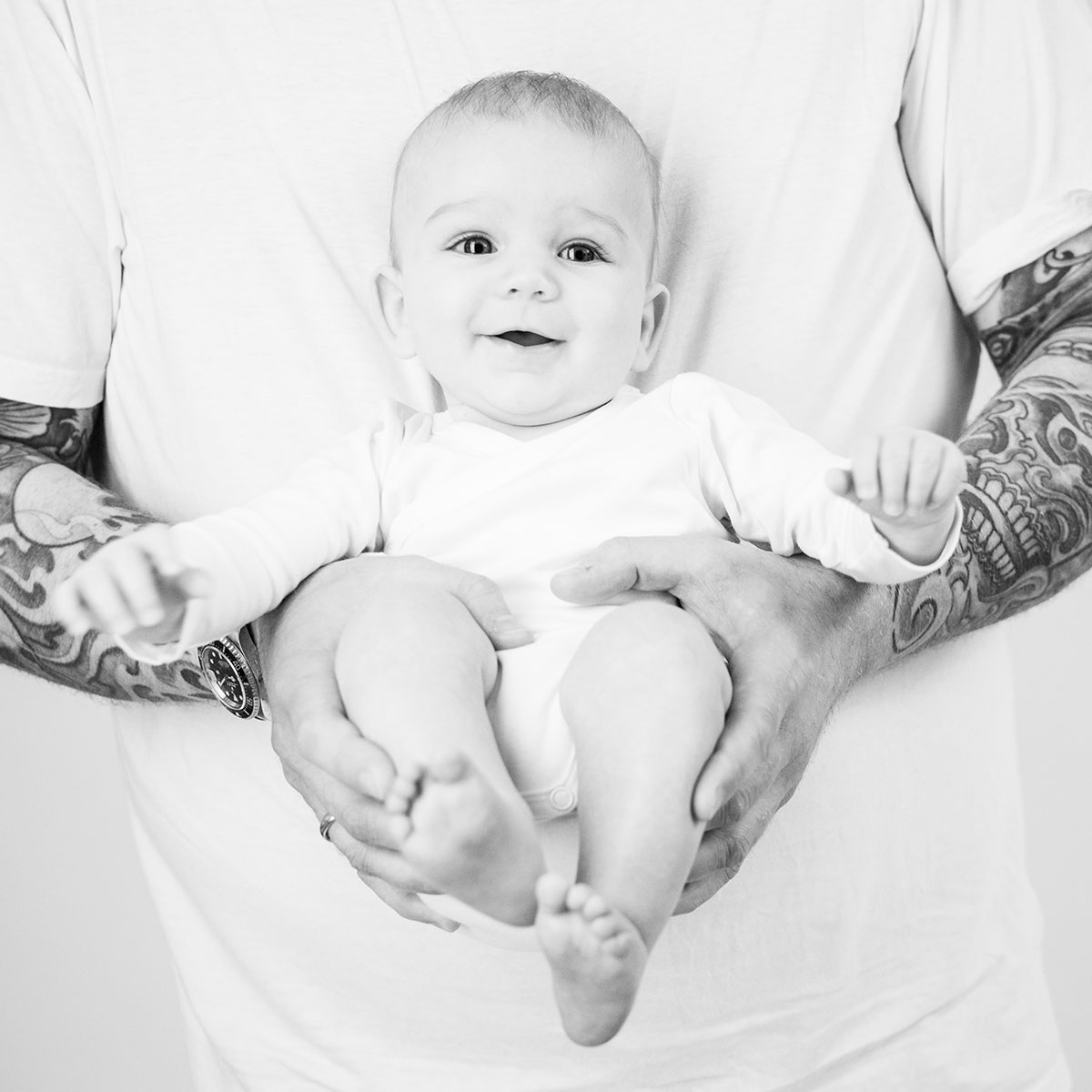 baby auf dem arm vor papas bauch, papa hat volltätowierte arme und das baby strahlt